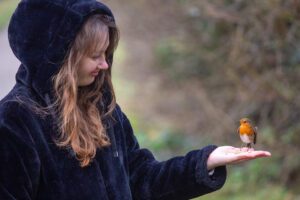 A photo of Sara - Artist at Dinky Drawings, with a robin sitting on her hand