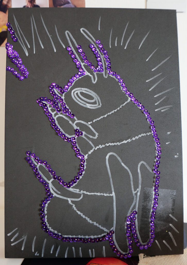 bee drawing in white on black foam block with pinned purple sequins.